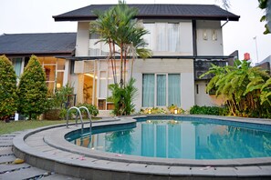 A swimming pool with a curved edge, surrounded by a stone deck. There are palm trees and other greenery around the pool area. - W Home Cipete (Jakarta)