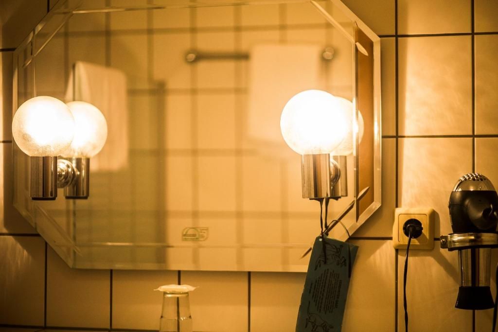 A bathroom with a large mirror, two wall-mounted lights, a hairdryer, and a soap dispenser.