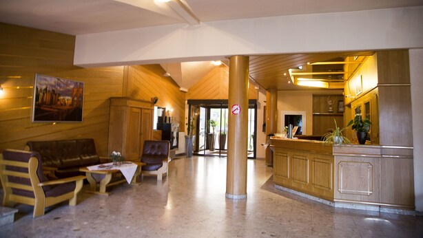 A lobby with wooden walls, a reception desk, a seating area with a sofa and chairs, and a large pillar. - Hotel Stadt Peine (Peine)