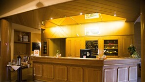 A reception area with a wooden counter, a coffee machine, a small table with a menu, and a potted plant. - Hotel Stadt Peine (Peine)