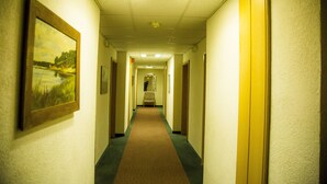 A hotel hallway with framed pictures on the walls, a carpeted floor, and doors on both sides. - Hotel Stadt Peine (Peine)