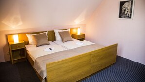 A neatly made bed with a wooden headboard, two bedside tables with lamps, and a framed picture on the wall. - Hotel Stadt Peine (Peine)