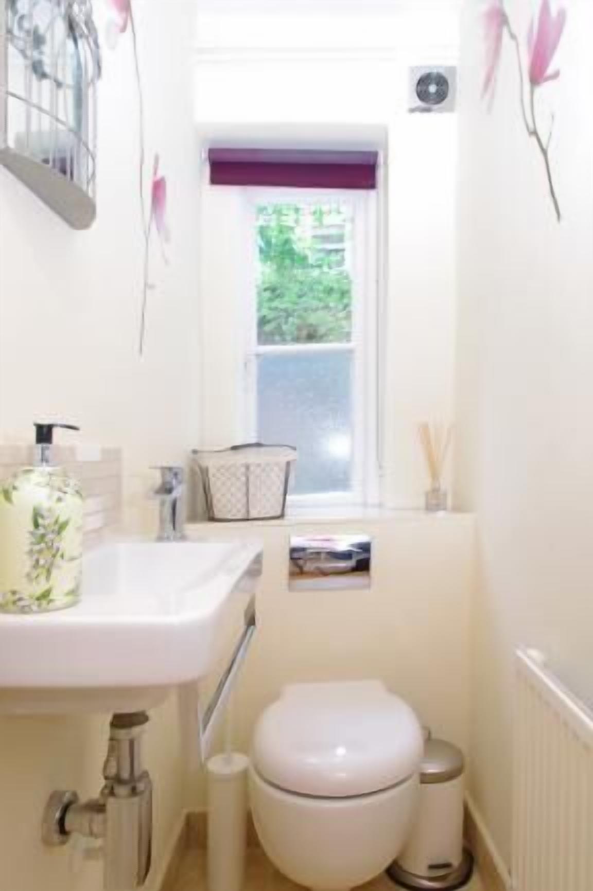 A small bathroom with a white sink, a toilet, and a window with a view of greenery outside.