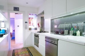 A modern kitchen with white cabinets, stainless steel appliances, and a sign reading "TO THE TRAINS".