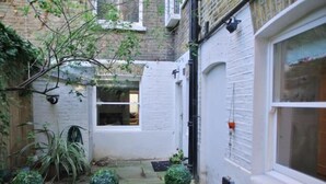 A narrow alleyway with a white door and a window, surrounded by brick walls and greenery.