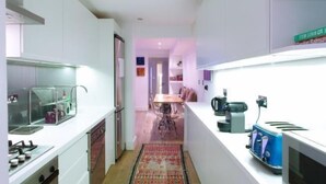A narrow kitchen with a dining area in the background, a microwave, and a coffee maker on the counter.