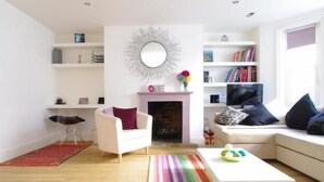 A modern living room with a fireplace, white sofas, a bookshelf, and a colorful striped rug.