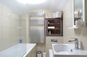 A bathroom with a bathtub, a sink, a mirror, a towel rack, and a toilet. - The London Agent Kensington Comeragh (London)
