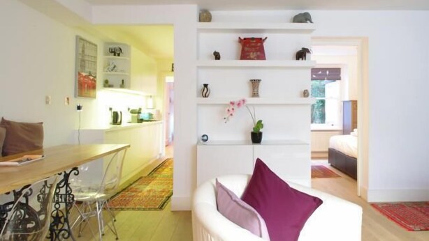 A modern living room with a white sofa, a dining table with chairs, and a kitchen area in the background.