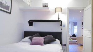 A neatly made bed with white and gray bedding, a black headboard, and a bedside lamp.