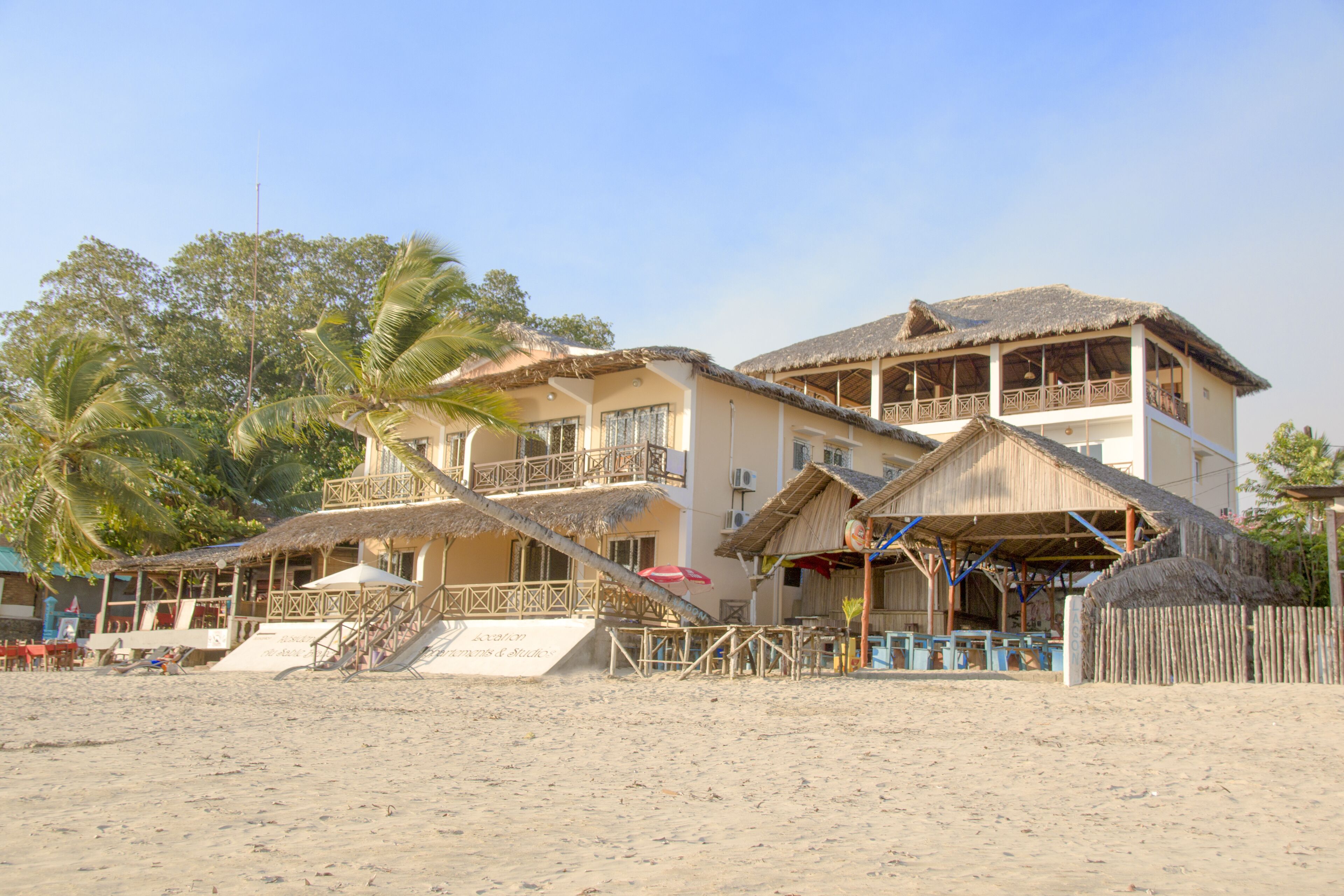 A beachfront hotel with multiple balconies, a thatched roof, and a sandy beach area.