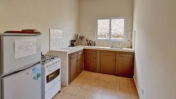 A kitchen with a refrigerator, stove, oven, and a window with a view of trees.