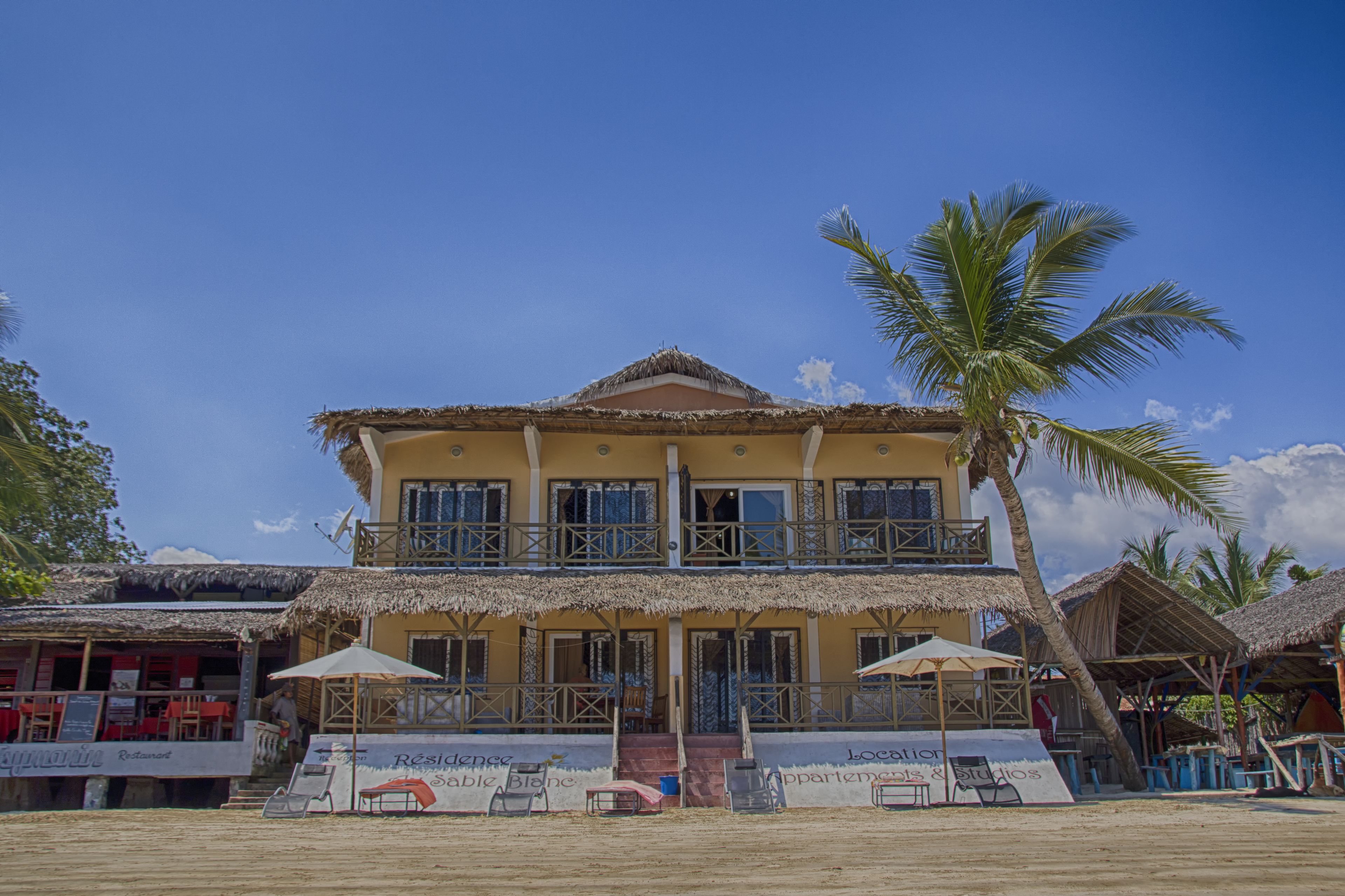 A two-story building with a thatched roof, balconies, and outdoor seating areas.