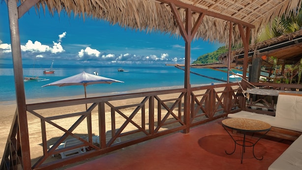 Un salon de plage avec vue sur la mer, doté d’un toit de chaume et d’une terrasse en bois.