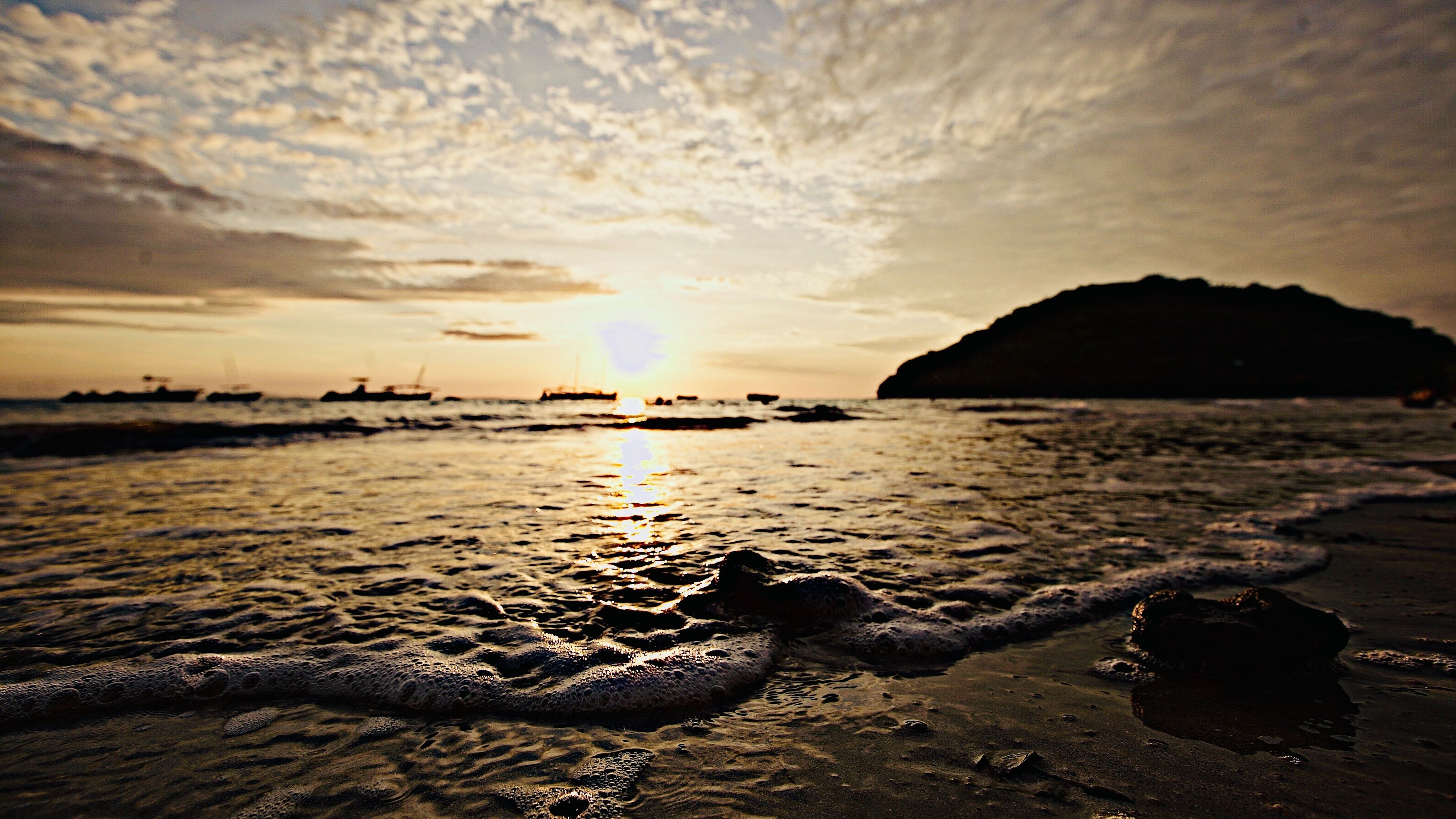 A beach with waves, a sun setting or rising, and a distant landmass.