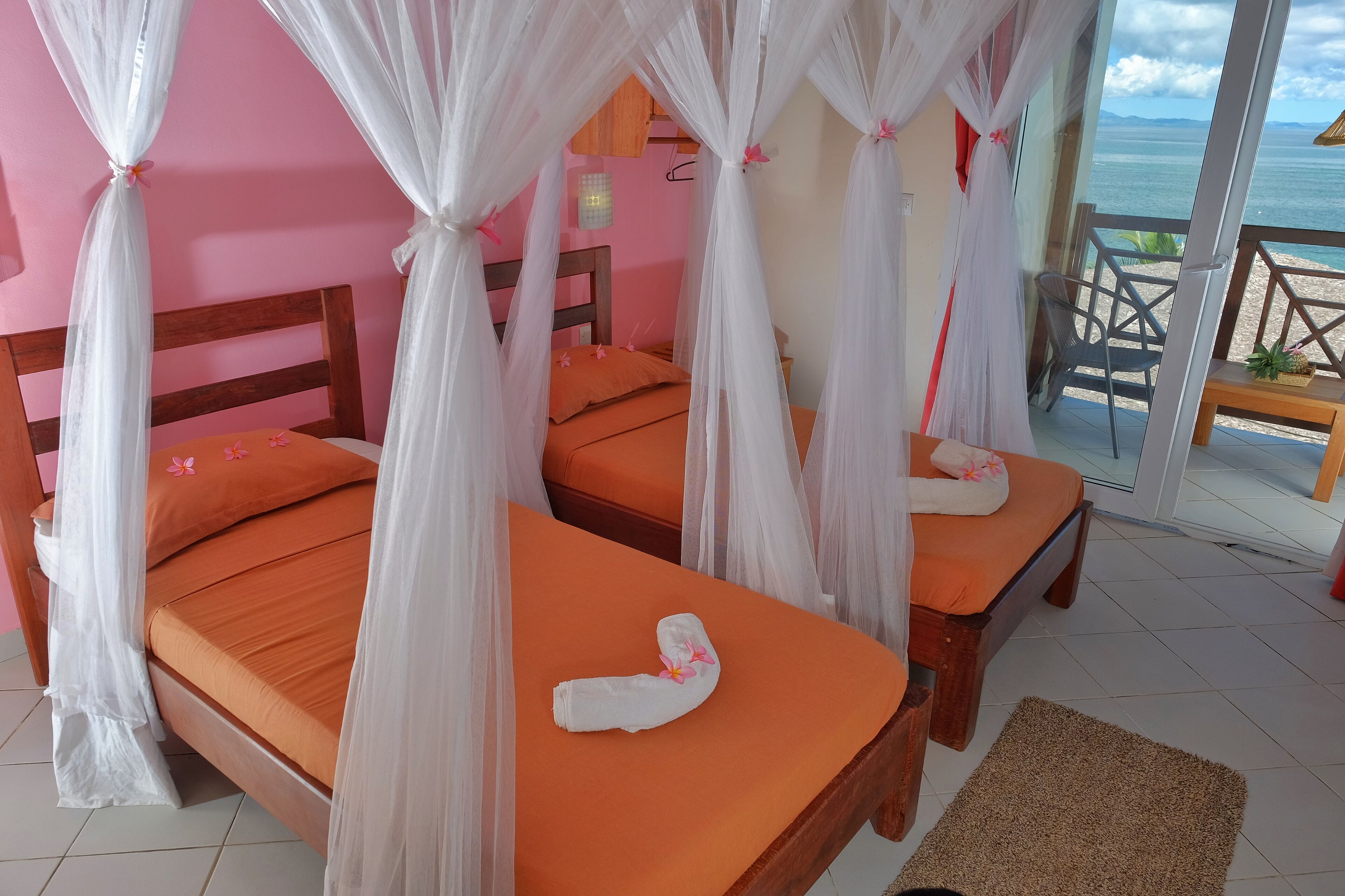 A room with two beds, each with an orange bedspread and white canopy.