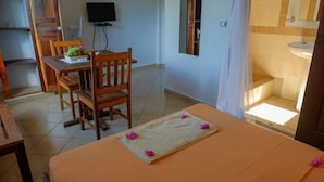 Un coin repas avec une table, des chaises, un téléviseur, et une salle de bain visible au fond.