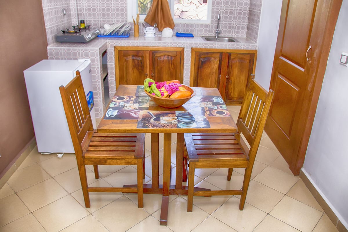 Een eetgedeelte met een houten tafel en stoelen, een schaal fruit en een koelkast.