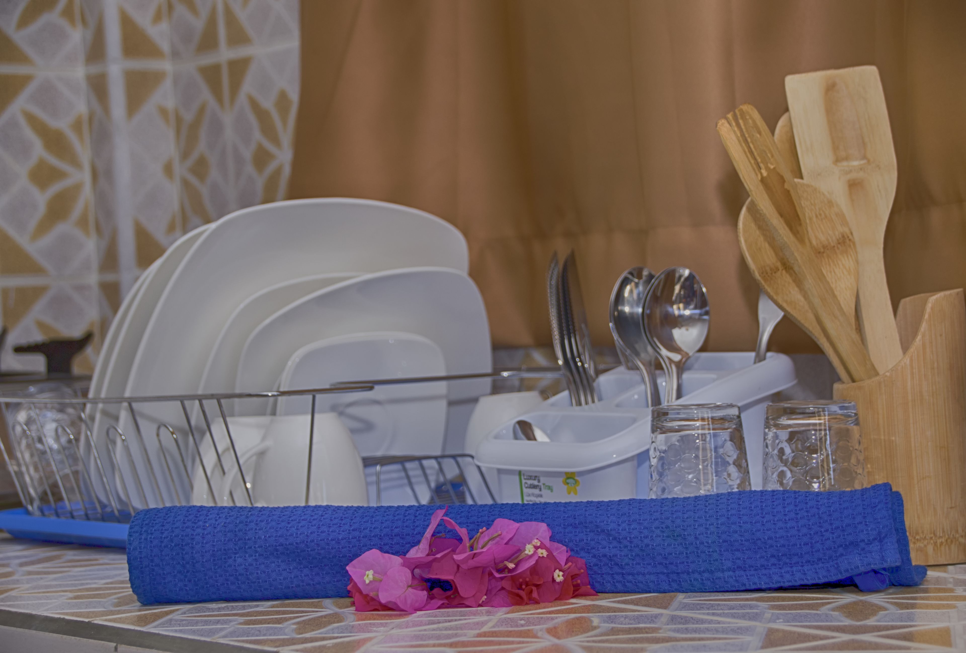 A table set with white plates, silverware, and glassware, with a blue napkin and a small pile of pink flowers.