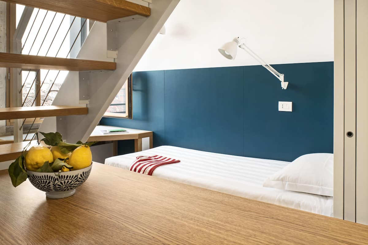 A room with a bed, a desk, a bowl of lemons, and a staircase.