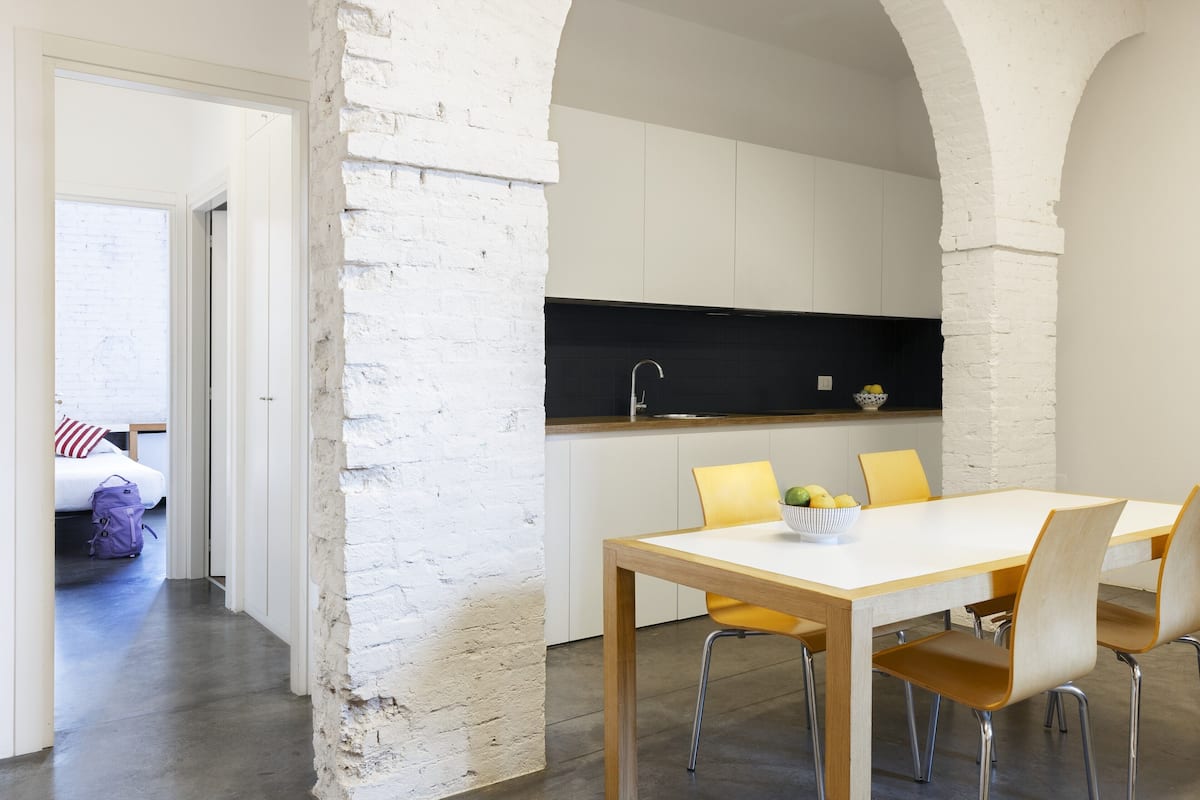 A modern kitchen with white cabinets, a black countertop, and a wooden dining table with yellow chairs.