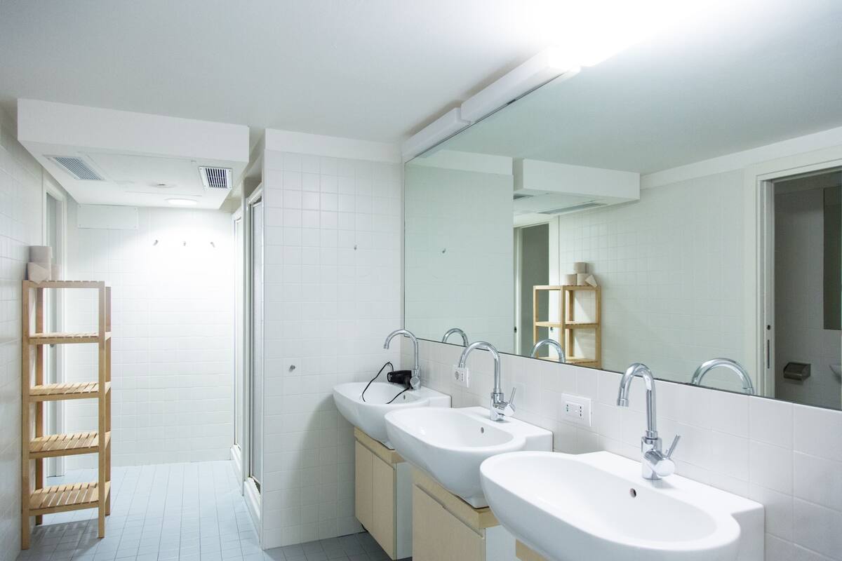 A modern bathroom with two sinks, a large mirror, and a wooden shelf.