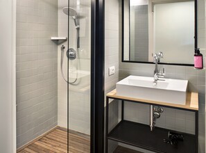 Un baño moderno con ducha envuelta en vidrio, un lavabo blanco y un espejo encima.