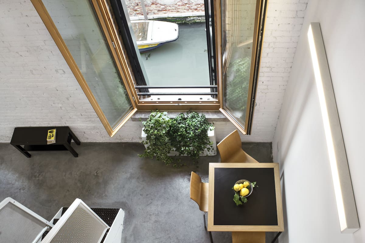 A room with a table, chairs, a potted plant, and a window with a view of a boat.