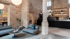 Ein großzügiger Lounge-Bereich mit Backsteinwand, einer Bar mit verschiedenen Flaschen und Sitzgelegenheiten, darunter Sofas und ein kleiner Tisch.