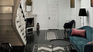Una sala de estar con chimenea, una araña, un sofá y un reloj.