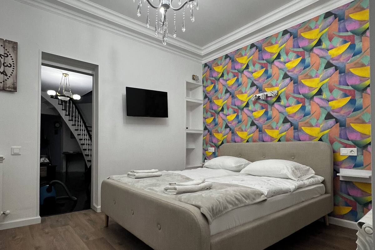Un dormitorio con cama, una araña, un televisor y una pared colorida.