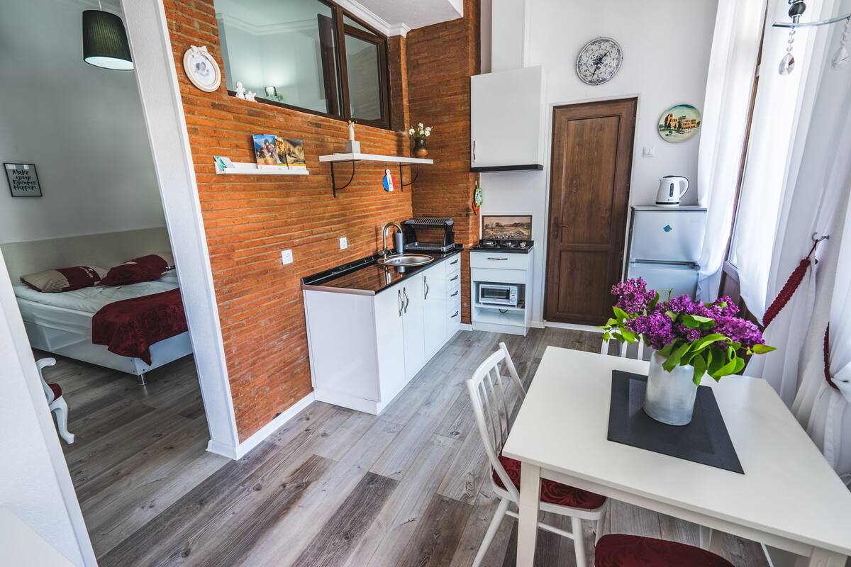 Una cocina compacta con armarios blancos, horno empotrado y refrigerador pequeño.