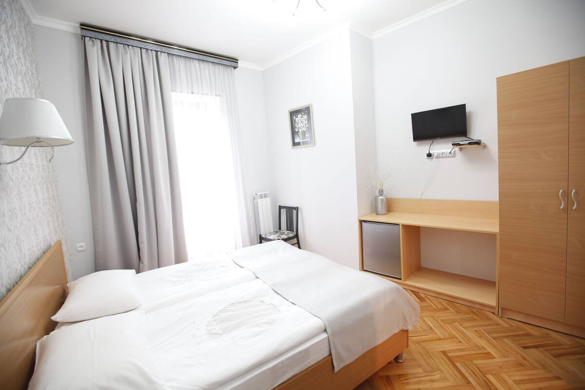 Un dormitorio ordenado con una cama, un televisor montado en la pared y un armario de madera.