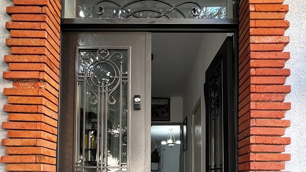 Una puerta con marco de metal decorativo, un vidrio y un muro de ladrillo.