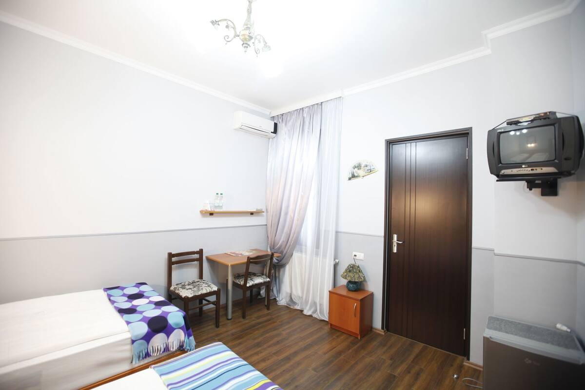 Una habitación pequeña y ordenada con una cama, dos sillas, una mesa, un televisor, una puerta y un armario pequeño.