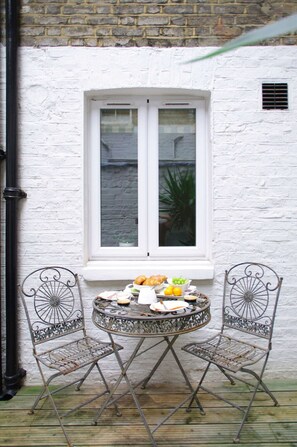 A round metal table with two chairs, a white window, and a small plant inside. - The London Agent Chelsea Finborough (London)