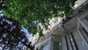 A building with a classical architectural style, featuring a balcony with a balustrade, large windows, and a visible tree canopy overhead. - The London Agent Chelsea Finborough (London)
