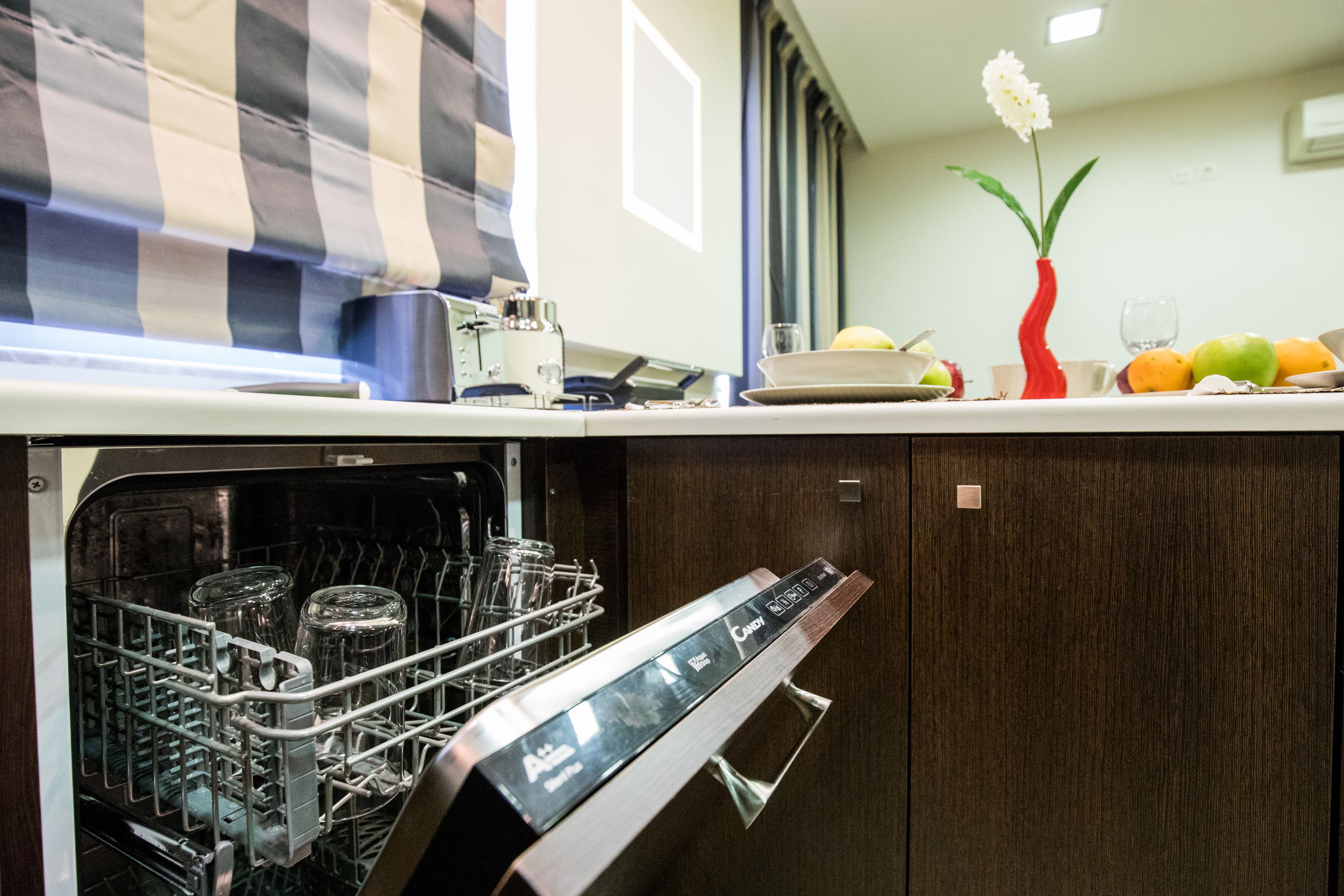 Una cucina con lavastoviglie, una tenda a righe e un vaso con fiori sul bancone.