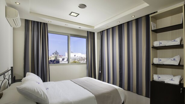 Ein Hotelzimmer mit Bett, Kleiderschrank, einem fenster mit Vorhängen und Blick auf Gebäude.
