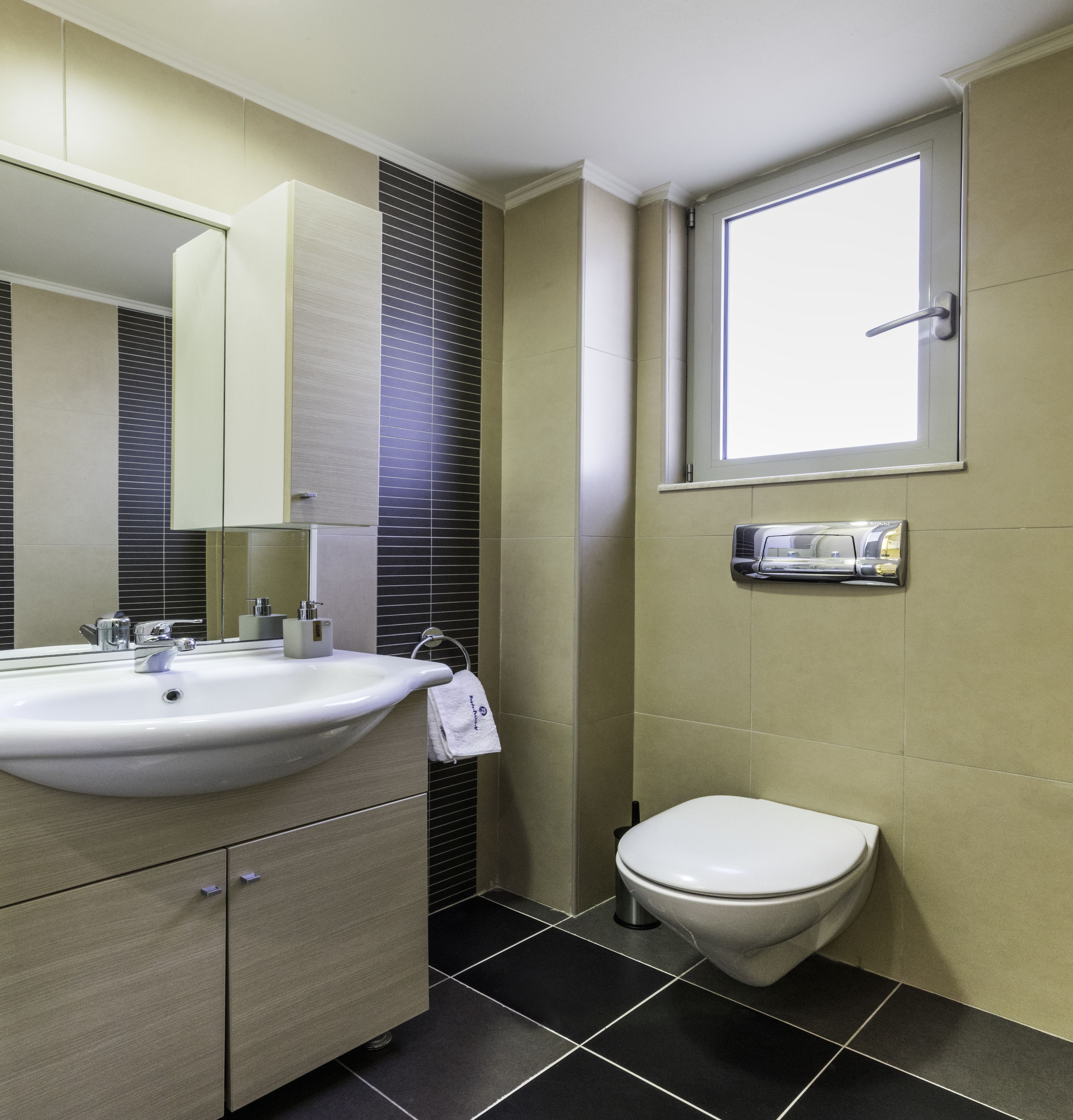 Ein modernes Badezimmer mit einem weißen Waschbecken, einer Toilette und einem Fenster über der Toilette.