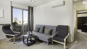 Ein modernes Wohnzimmer mit einem grauen Sofa, zwei Sesseln, einem kleinen Tisch mit Flasche und Gläsern und einer Glastür, die auf einen Balkon führt.