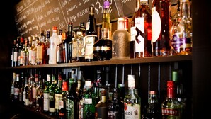 Bar com estantes cheias de garrafas de bebidas alcoólicas diversas.