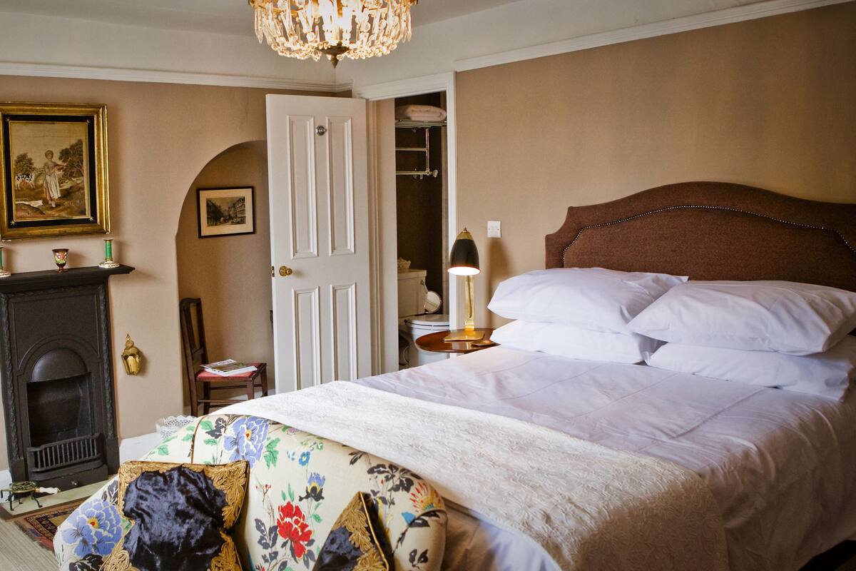A bedroom with a bed, a desk, a chair, a fireplace, and a door leading to a closet.