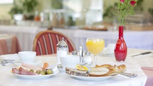 A breakfast table with plates of food, a glass of orange juice, and a vase of flowers. - Hotel Drei Morgen (Leinfelden-Echterdingen)