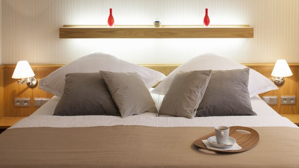 A neatly made bed with a brown bedspread, two bedside lamps, and a tray with a cup and saucer on the bed. - Hotel Drei Morgen (Leinfelden-Echterdingen)