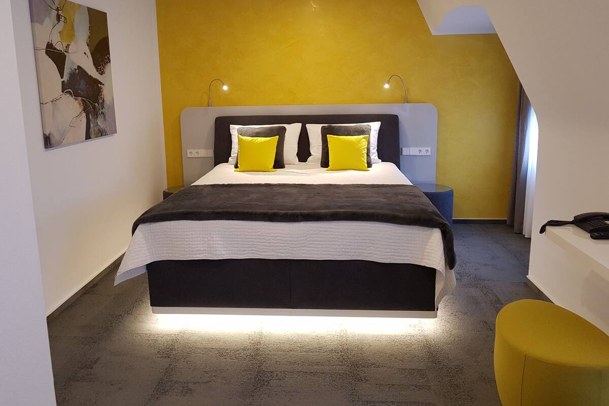 A modern bedroom with a bed, two bedside lamps, a painting, and a telephone on a desk.