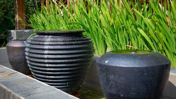 Tres macetas grandes y negras con agua y plantas verdes en un jardín.