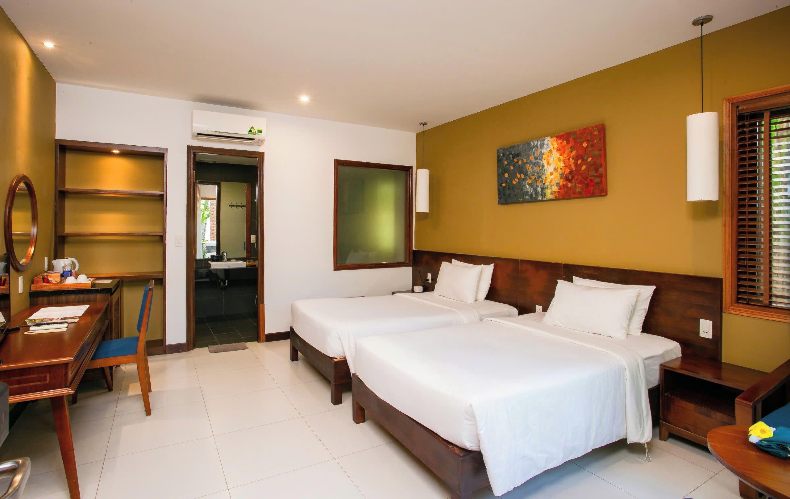A hotel room with two beds, a desk, a chair, and a painting on the wall.
