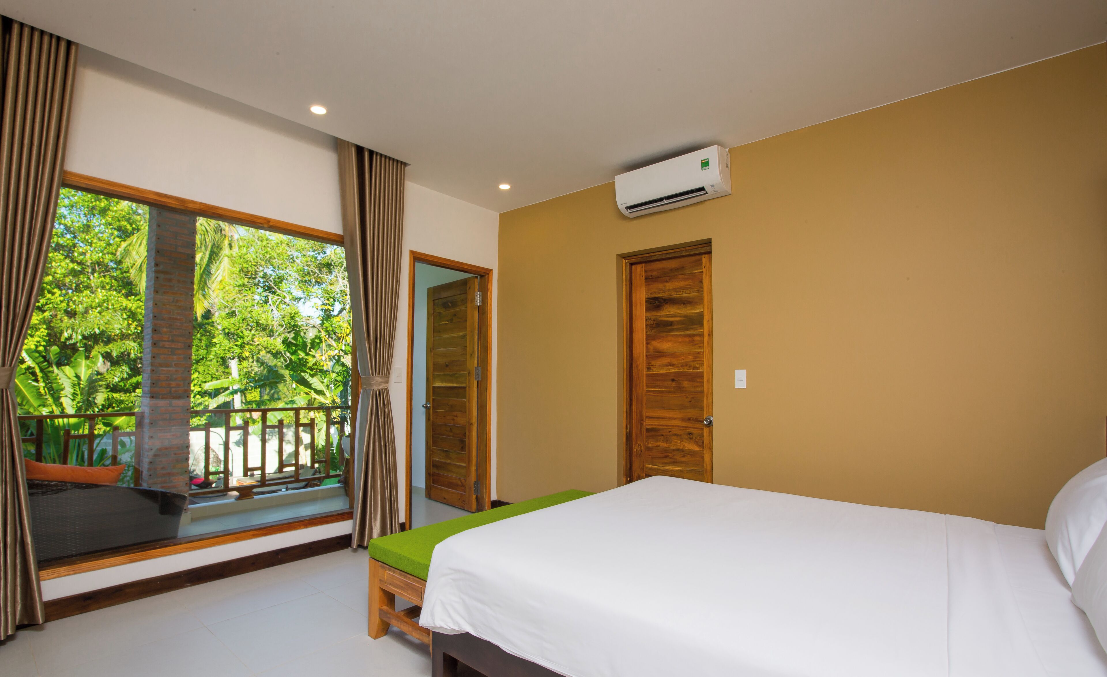 A bedroom with a bed, a window with curtains, a door, and an air conditioning unit.
