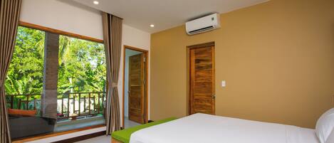 A bedroom with a bed, a window with curtains, a door, and an air conditioning unit.